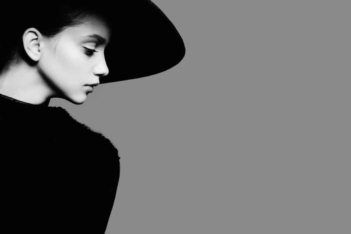 Afbeeldingen van Portrait of beautiful girl in hat in profile posing in studio black and white photography
