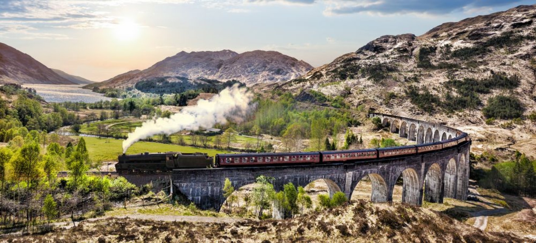 Afbeeldingen van Glenfinnan Railway Viaduct in Scotland with the Jacobite steam train against sunset over lake