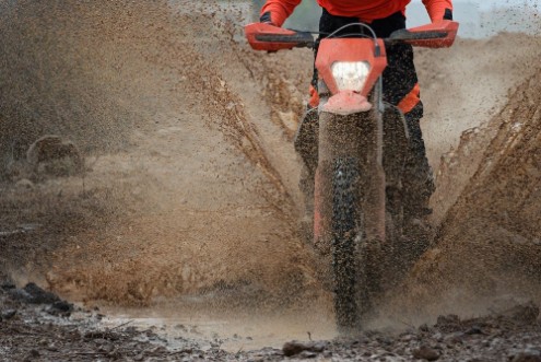 Picture of Motocross driver splashing mud on wet and muddy terrain