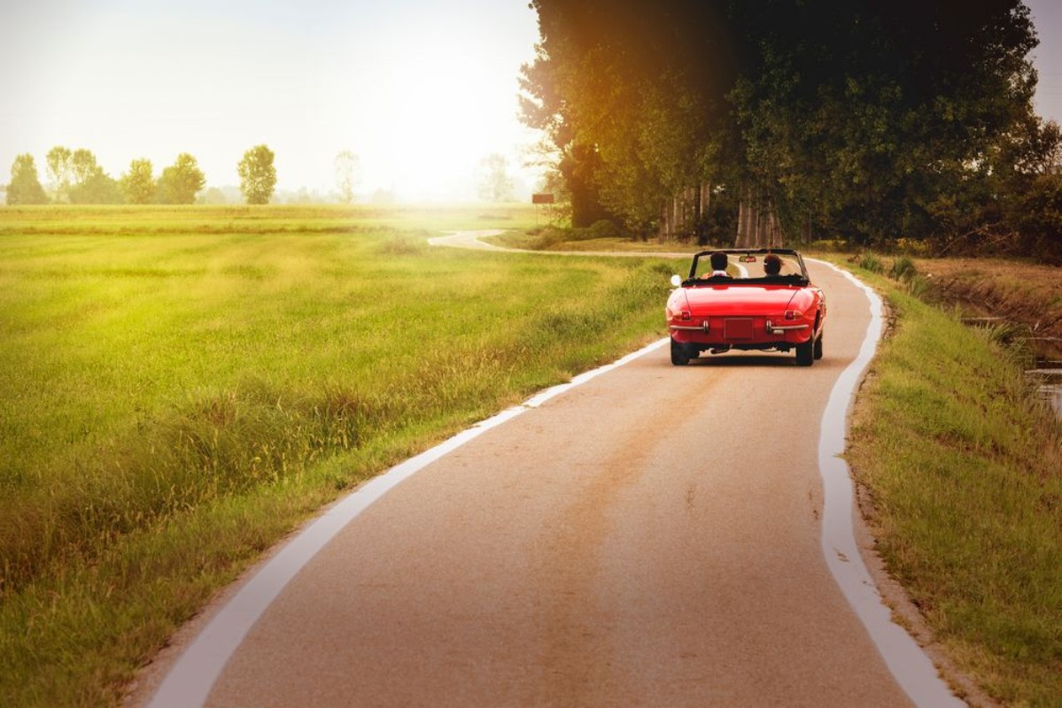 Image de Classic red convertible car traveling in the countryside at sunset