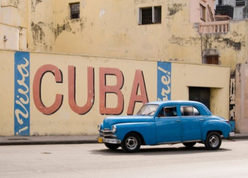 Picture of A vintage 1950s American car passing a Viva Cuba sign painted on a wall in cental Havana Cuba