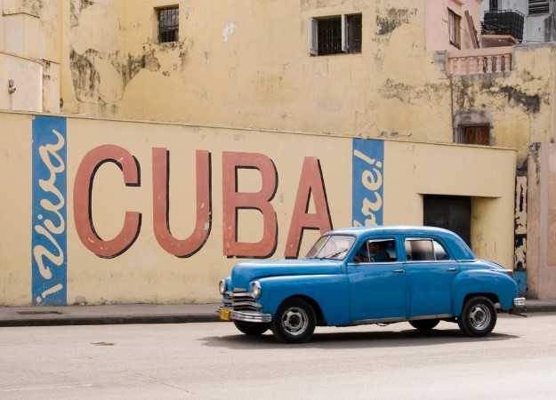 Afbeeldingen van A vintage 1950s American car passing a Viva Cuba sign painted on a wall in cental Havana Cuba
