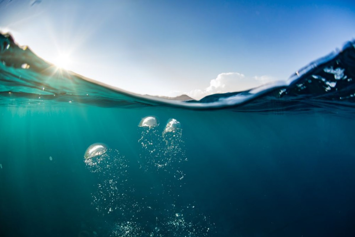 Afbeeldingen van Ocean water line splits sky and underwaer part Air bubbles in deep blue Bright sun light and blue clear sky