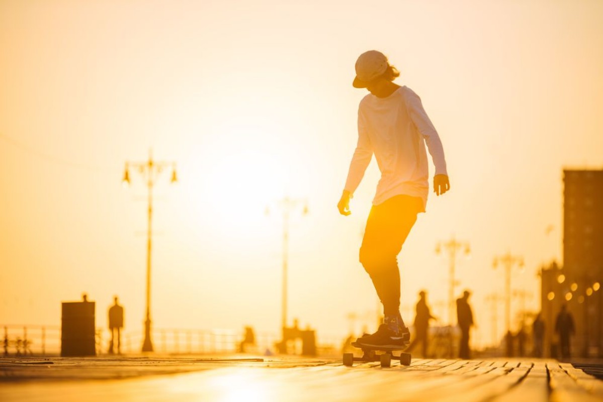 Afbeeldingen van Silhouette of young boy riding longboard on the boardwalk summer time sunset