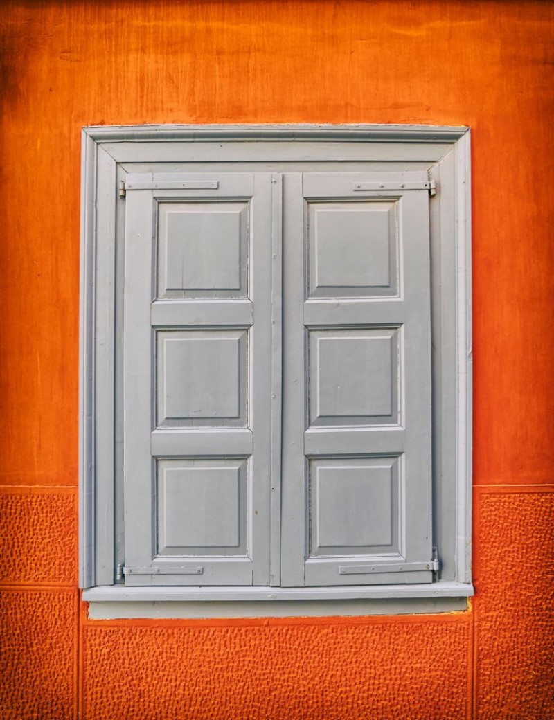 Afbeeldingen van Grey closed shutters window on vibrant orange wall filtered