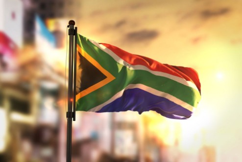 Afbeeldingen van South Africa Flag Against City Blurred Background At Sunrise Backlight