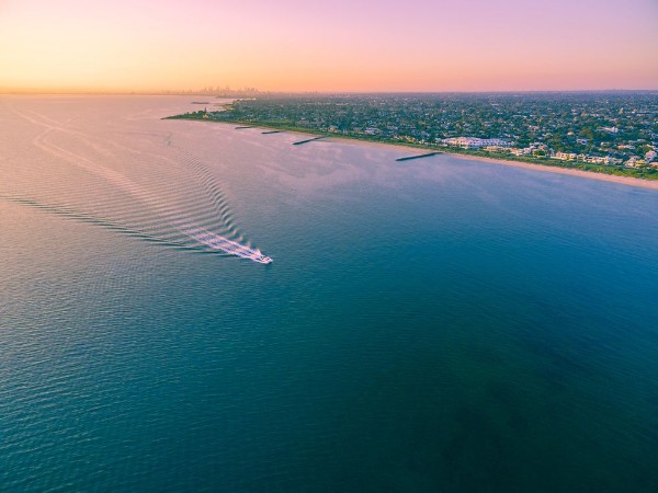 Afbeeldingen van Aerial view of boat sailing across Port Phillip bay with Melbourne coastline and suburban areas in the background at beautiful sunset