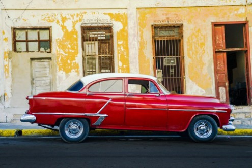 Afbeeldingen van Vibrant red shiny car and ruined house in Cuba