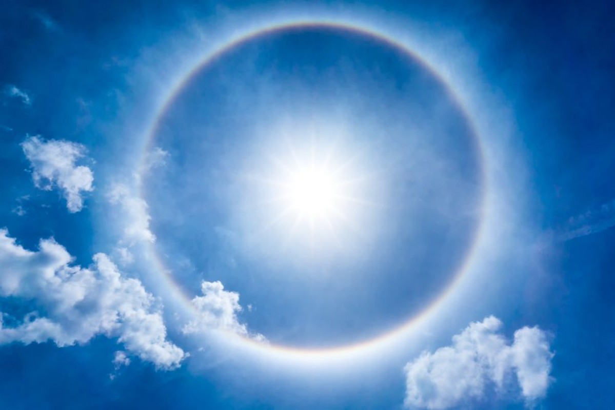 Afbeeldingen van The storng sun halo at noon time on the blue sky and cumulus clouds