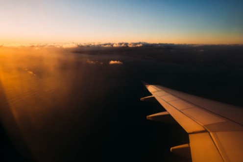Picture of View from airplane window above Portugal at sunset Sun shining from the corner of image on the aircraft wing with large water space beneath