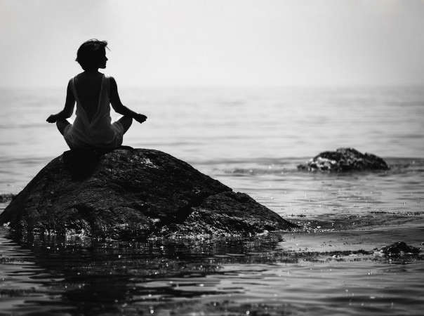 Afbeeldingen van Young woman sits in a lotus position on a large stone in the sea and meditates her fingers are folded in Prithivi mudra