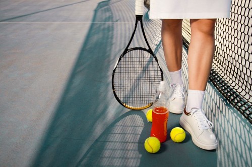 Afbeeldingen van Tennis concept  woman legs next to tennis balls and refreshing drink next to net  copy space  outdoors 