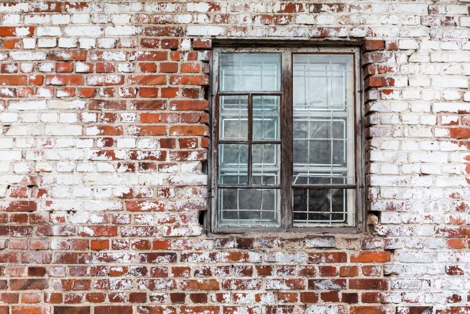 Afbeeldingen van Wooden window on weathered red brick wall painted white