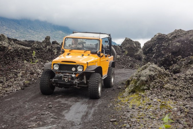 Picture of A curly-haired man is looking away driving an offroad yelow vehicle at the top of a valley with dark ground road
