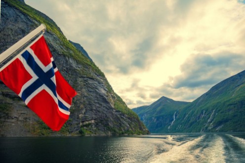 Afbeeldingen van Mountain landscape with cloudy sky Majestic Geiranger fjord  View from ship Norvegian flag against beautiful nature of Norway