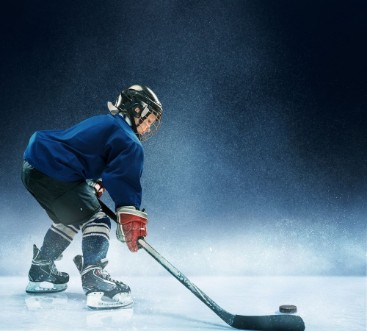 Bild på Little boy playing ice hockey at arena A hockey player in uniform with equipment over a blue background The athlete child sport action concept