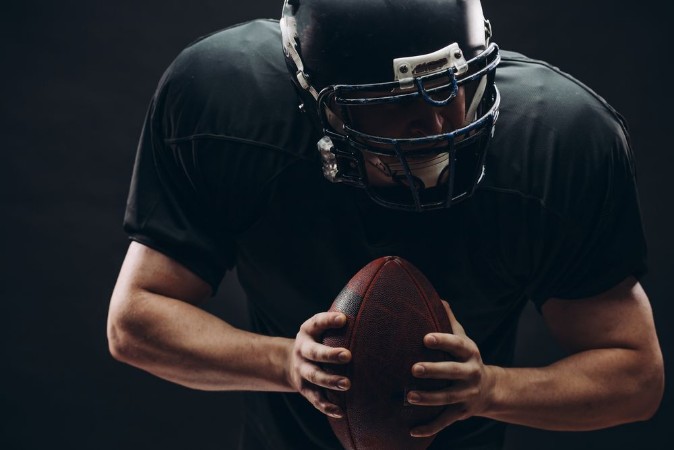Bild på American football player with black helmet and armour running in motion holding ball getting ready to score a goal close up shot over dark background
