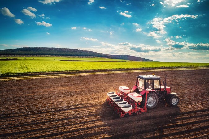 Afbeeldingen van Farmer with tractor seeding crops at field aerial drone view