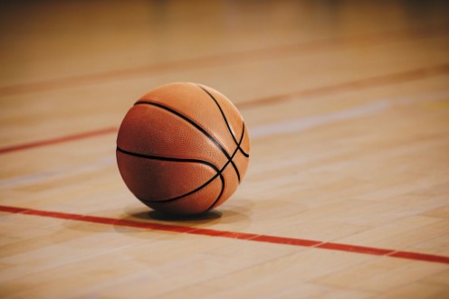 Picture of Classic Basketball on Wooden Court Floor Close Up with Blurred Arena in Background Orange Ball on a Hardwood Basketball Court