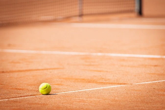 Afbeeldingen van Yellow tennis ball on orange sand and white lines