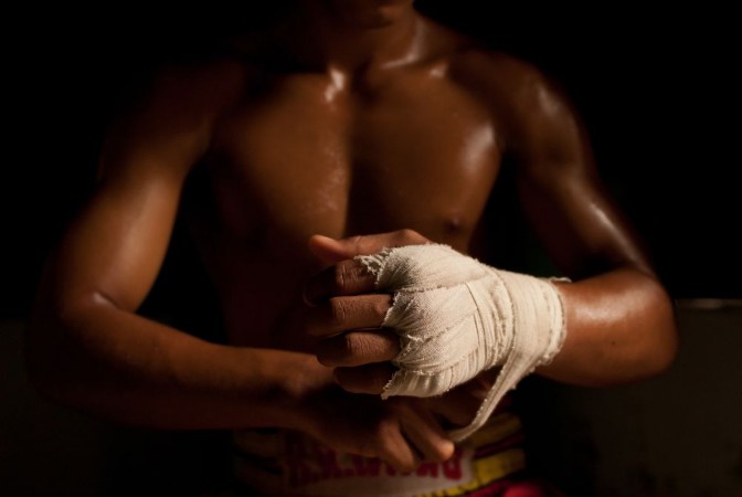 Bild på The muscular fighter tying tape around his hand preparing to box