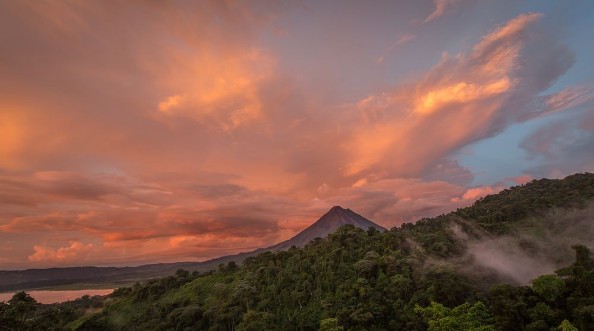 Afbeeldingen van Sunset on Lake Arenal and Arenal Volcano in Costa Rica brings Shades of red and orange as clouds rise from the jungle floor