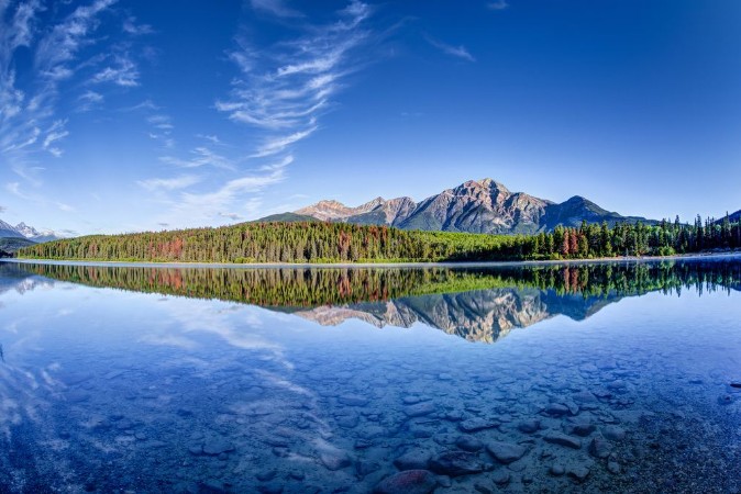Bild på Colorful trees lined the shores of Patricia Lake at Jasper National Park with Pyramid Mountain in the background The calm lake reflects a mirror image of the mountains and trees